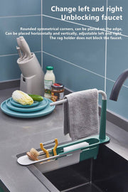 Adjustable telescopic sink rack in green and white, mounted over a kitchen sink, holding a towel, sponge, brush, and utensils for organized storage.