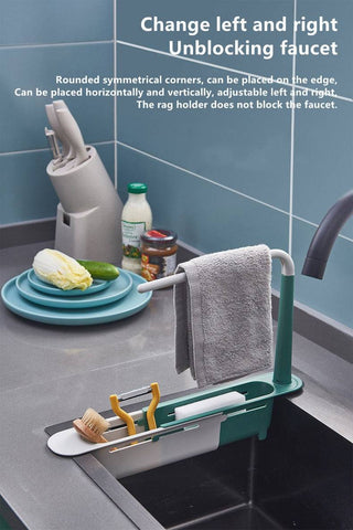 Adjustable telescopic sink rack in green and white, mounted over a kitchen sink, holding a towel, sponge, brush, and utensils for organized storage.