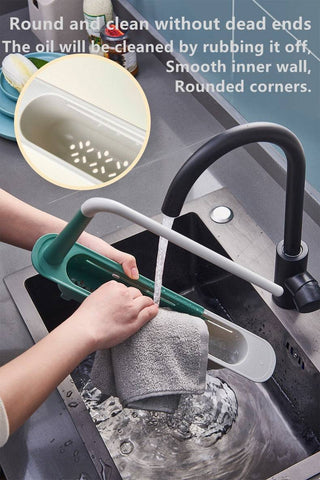 Adjustable telescopic sink rack in green and white, mounted over a kitchen sink, holding a towel, sponge, brush, and utensils for organized storage.