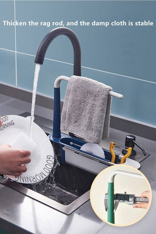 Adjustable telescopic sink rack in green and white, mounted over a kitchen sink, holding a towel, sponge, brush, and utensils for organized storage.